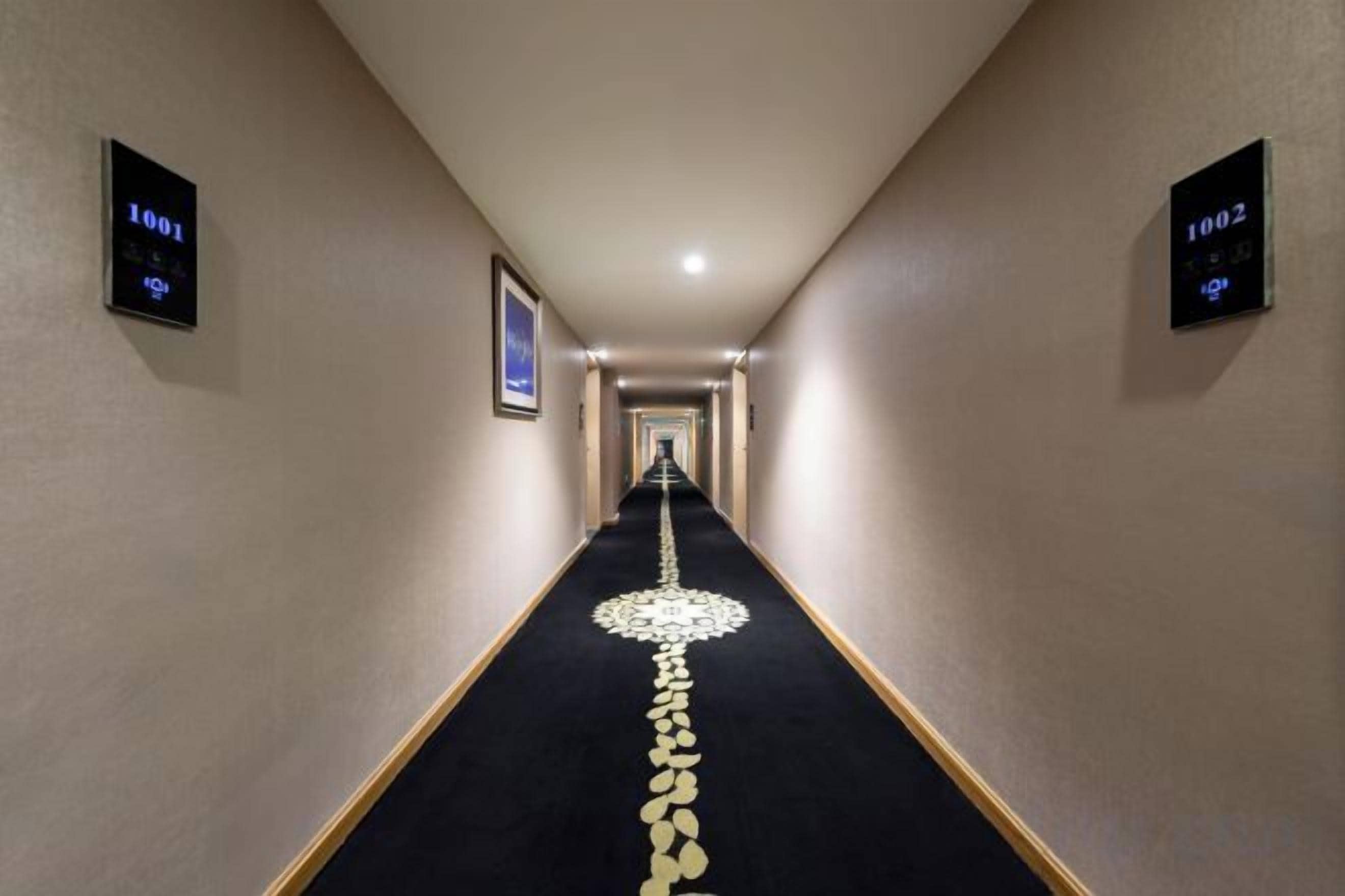 Un pasillo de hotel con piso alfombrado, puertas numeradas y un cuadro en la pared.