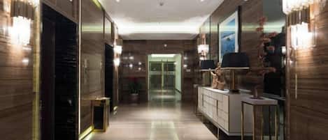 A hallway with a marble floor, a reception desk, and a large mirror.