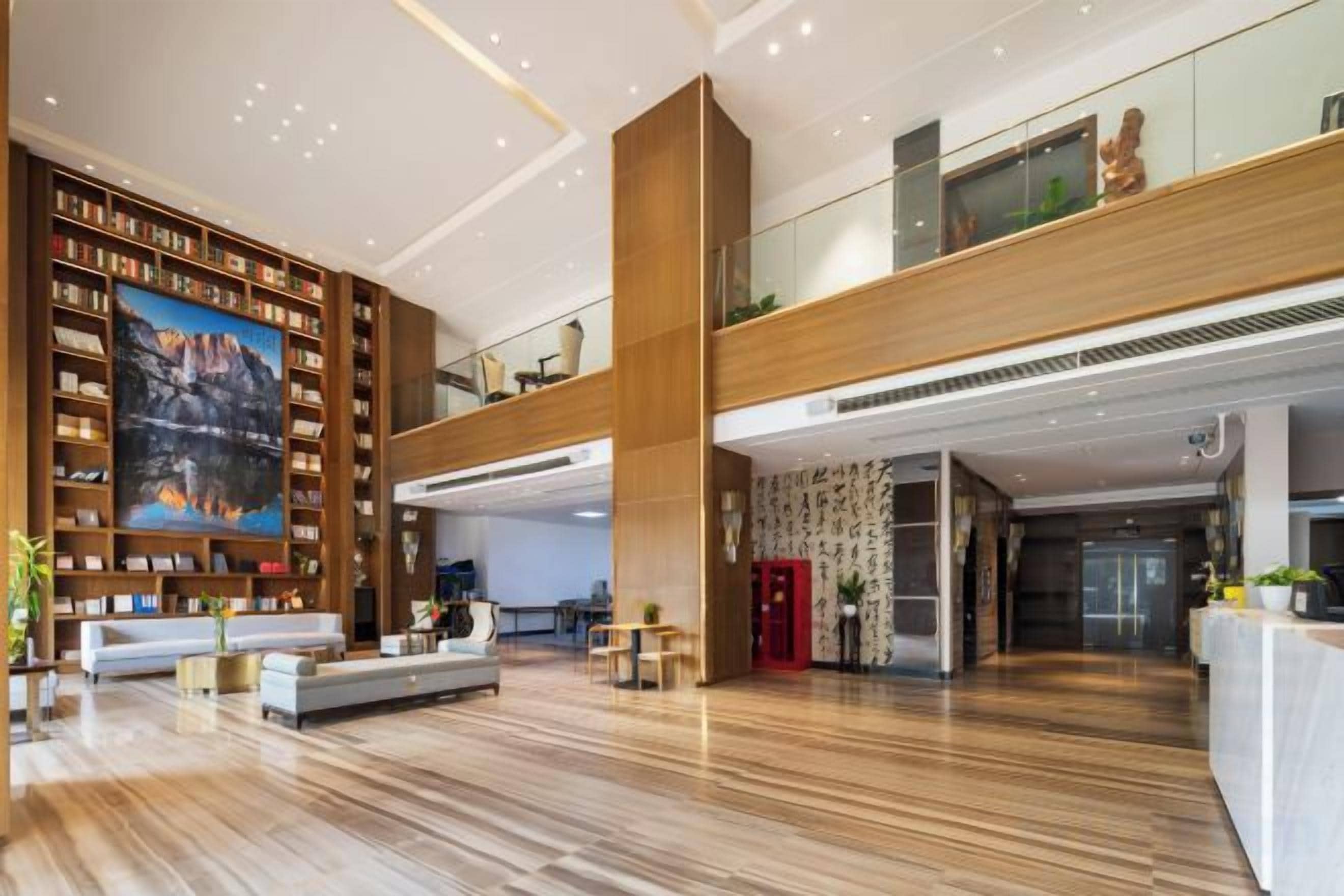 A spacious lobby with a high ceiling, a wooden reception desk, a seating area with sofas, and a large bookshelf.