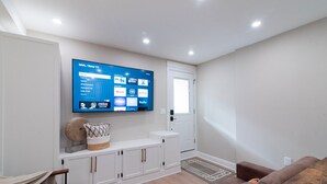 Uma sala de estar moderna com uma TV de tela plana na parede, um console de mesa branco, um sofá de couro marrom e piso de madeira.