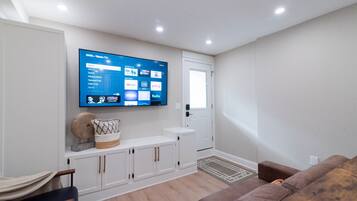 A modern living room with a flat-screen TV mounted on the wall, a white console table, a brown leather sofa, and a wooden floor.