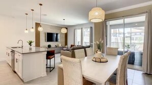 Une cuisine moderne dotée d’un îlot central, d’un coin repas avec des chaises en osier et de grandes fenêtres offrant une vue dégagée.