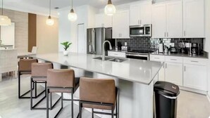 Une cuisine moderne avec des armoires blanches, des appareils en acier inoxydable et des luminaires suspendus.