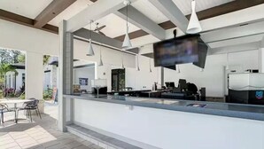 Un espace bar extérieur moderne, doté d’un comptoir, de luminaires suspendus et d’un écran de télévision.