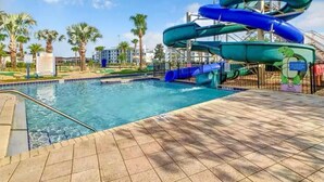 Une piscine avec un toboggan aquatique, des palmiers et un ciel dégagé.