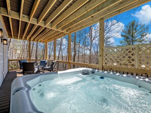 Ein Whirlpool auf einer Holzterrasse mit Blick auf Bäume und einen klaren Himmel.