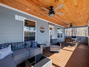 Eine überdachte Veranda mit einer grauen Couch, Korbstühlen, einem Esstisch und Deckenventilatoren.