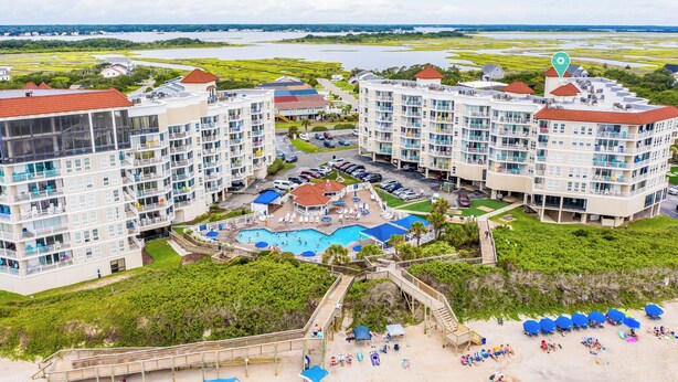 Ein Resort mit mehreren Gebäuden, einem zentralen Poolbereich und einem Strand mit Sonnenschirmen.