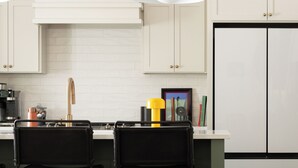 Una cucina moderna con mobili bianchi, sgabelli da bar neri, una sedia blu e un tavolino laterale nero.