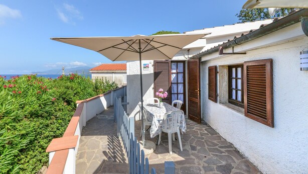 Eine Terrasse mit Tisch und Stühlen, einem großen Sonnenschirm und Blick auf das Meer.