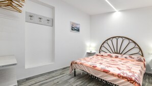 Ein Schlafzimmer mit Bett, Holzboden, Wandhandtuchhaltern, einem Nachttisch mit Lampe und einem gerahmten Bild an der Wand.