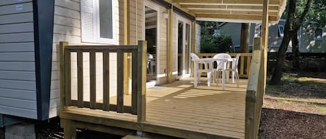 A wooden deck with a covered patio area, a small table with chairs, and a step leading to a door.