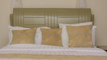 A bed with a green headboard, white bedding, and three beige pillows with "NIBA HOTEL" text.