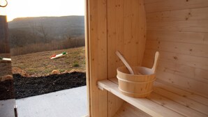 A wooden sauna with a view of a grassy field and hills.