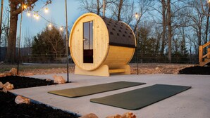 A wooden barrel structure with a door, surrounded by outdoor exercise mats and rocks.