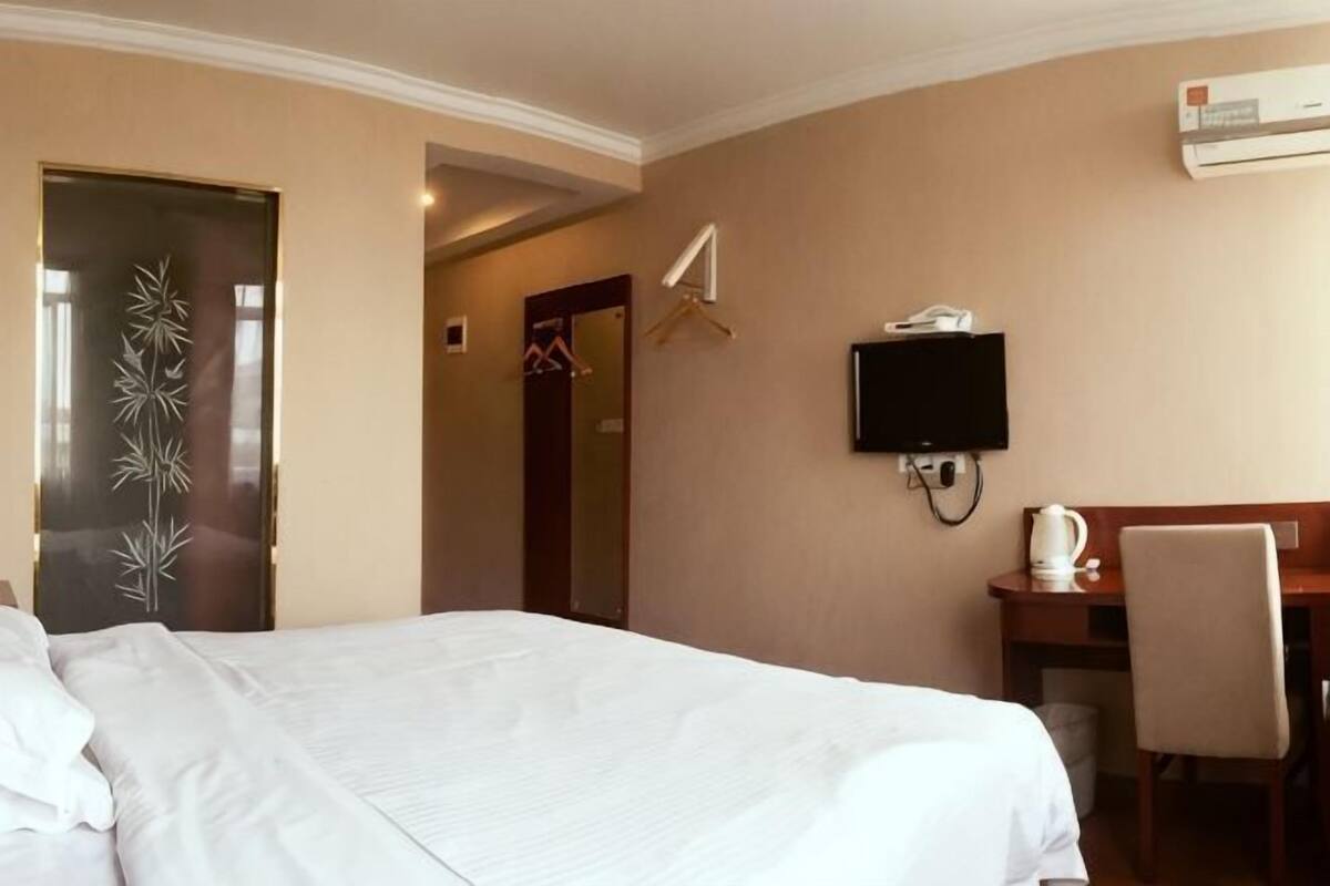 Ein Hotelzimmer mit einem Bett, einem Schreibtisch mit Stuhl, einem Fernseher und einer Klimaanlage.