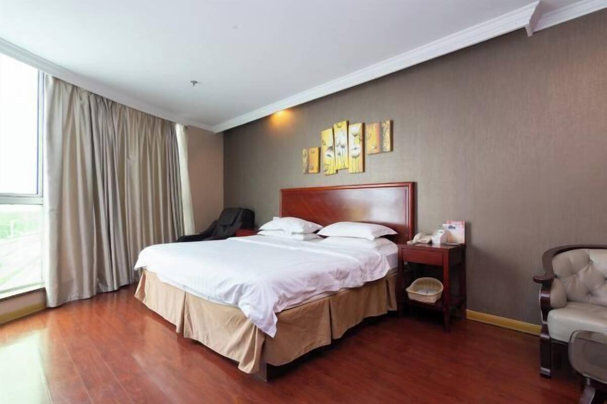 Ein Hotelzimmer mit Bett, Nachttisch, Stuhl, einem Fenster mit Vorhängen und Bildern an der Wand.