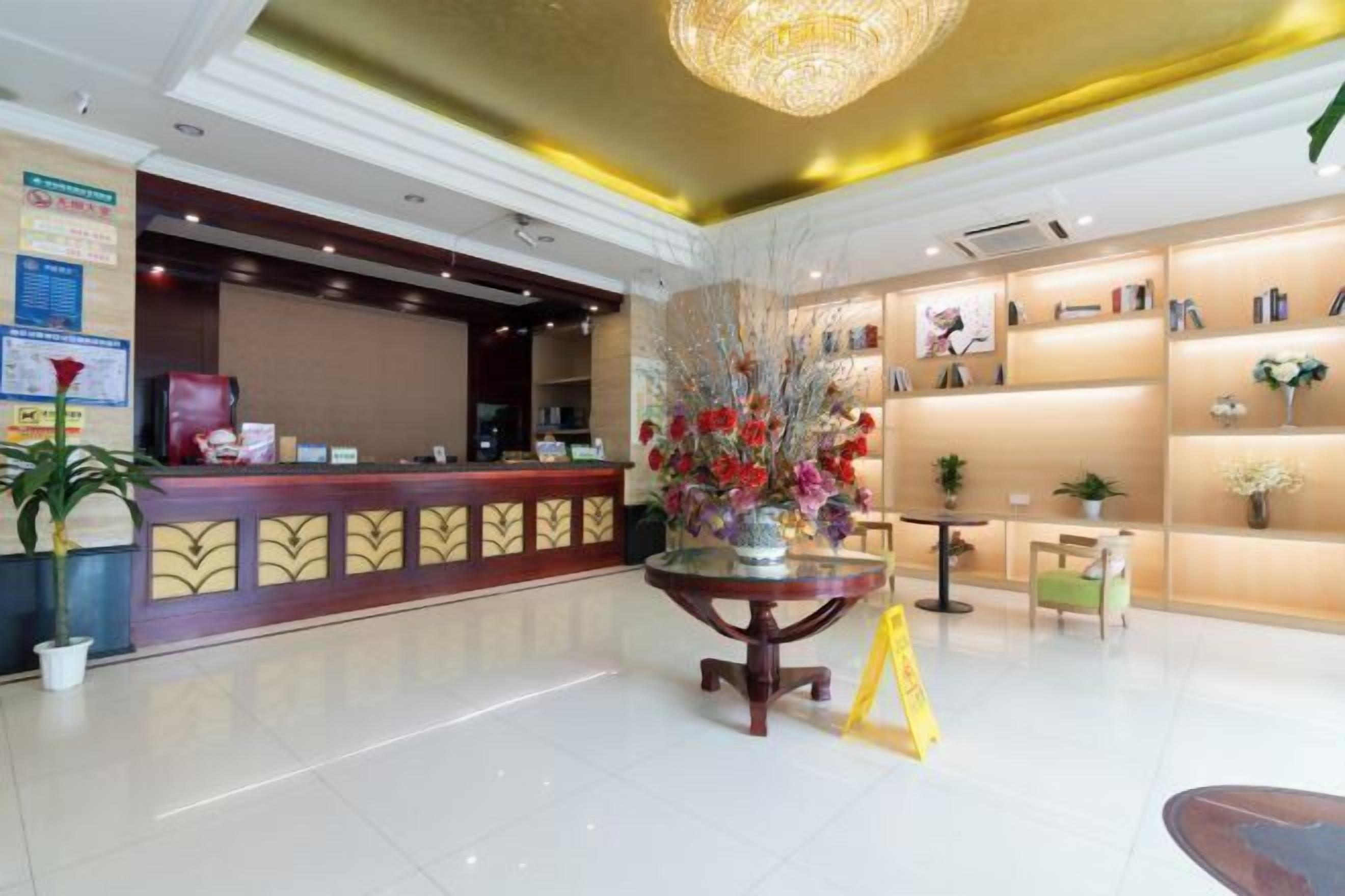 Un hall d’hôtel comprenant un comptoir d’accueil, une table ronde agrémentée d’un arrangement floral et une bibliothèque avec des photos encadrées.
