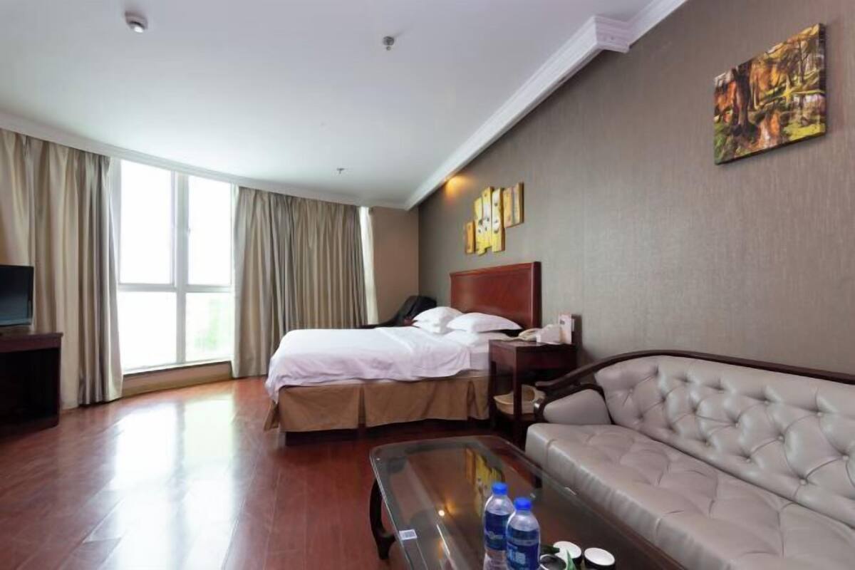 Ein Hotelzimmer mit Bett, Sofa, einem Glastisch, einem Fernseher und einem großen Fenster mit Vorhängen.