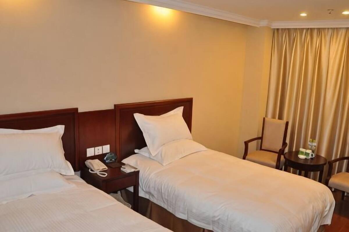 Ein Hotelzimmer mit zwei Einzelbetten, einem Nachttisch mit Telefon, einem Sessel und einem kleinen Tisch mit Lampe.