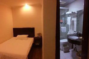 A hotel room with a bed, a nightstand, a bathroom with a sink and toilet.