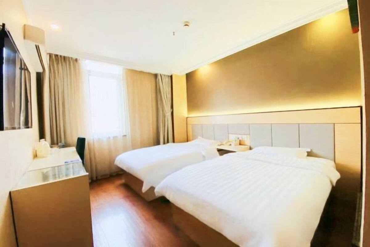 Ein Hotelzimmer mit zwei Betten, einem Schreibtisch, einem Spiegel und einem Fenster mit Vorhängen.