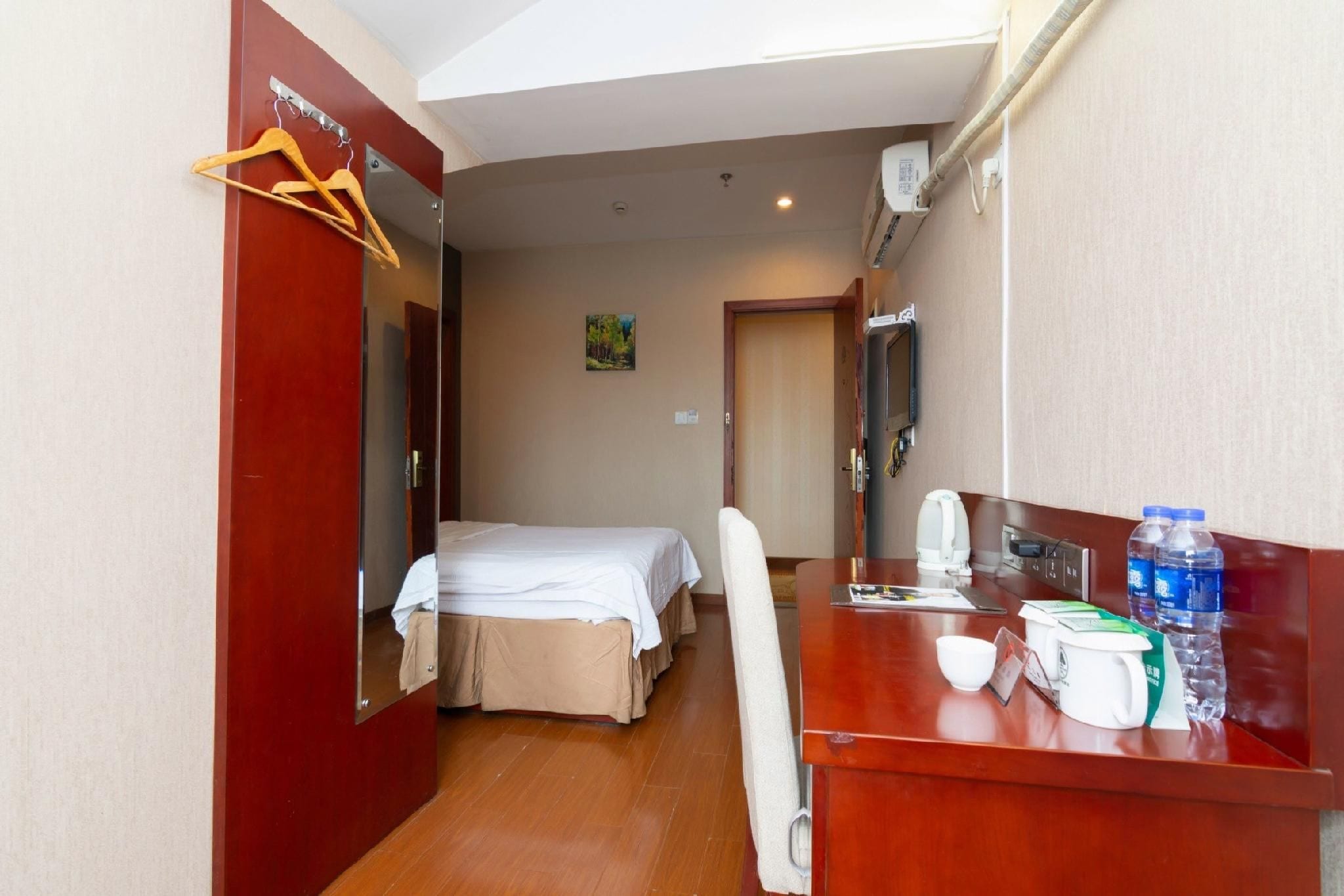 A hotel room with a bed, a desk with a coffee maker, and a mirror.