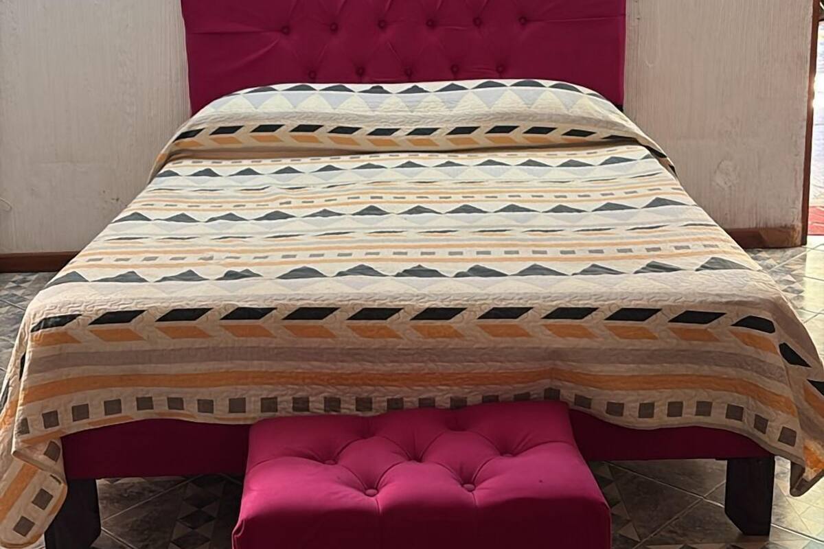 Un lit avec une couvre-lit à motifs et une tête de lit rembourrée de couleur rose.