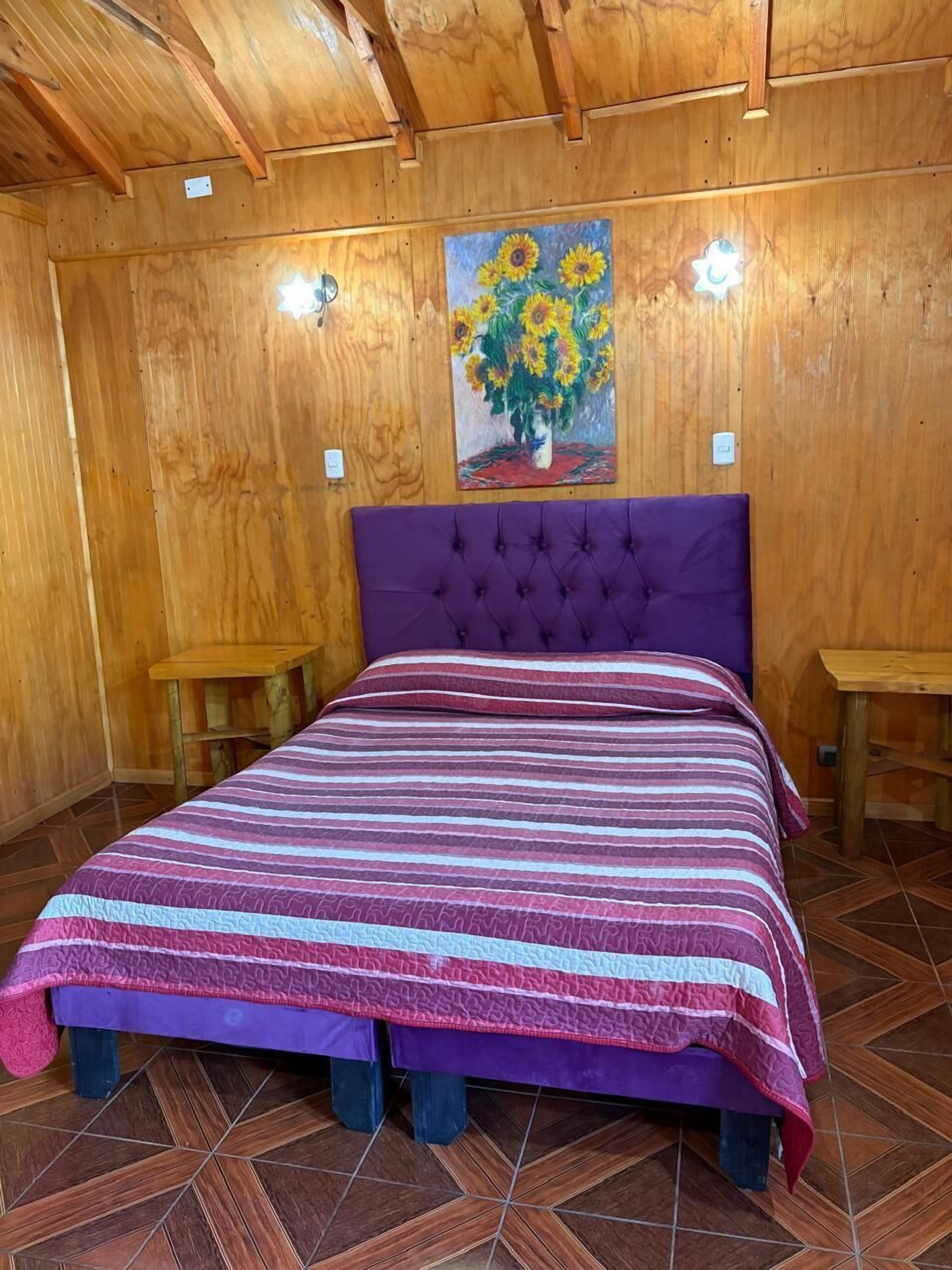 A wooden room with a bed, two nightstands, and a painting of sunflowers.