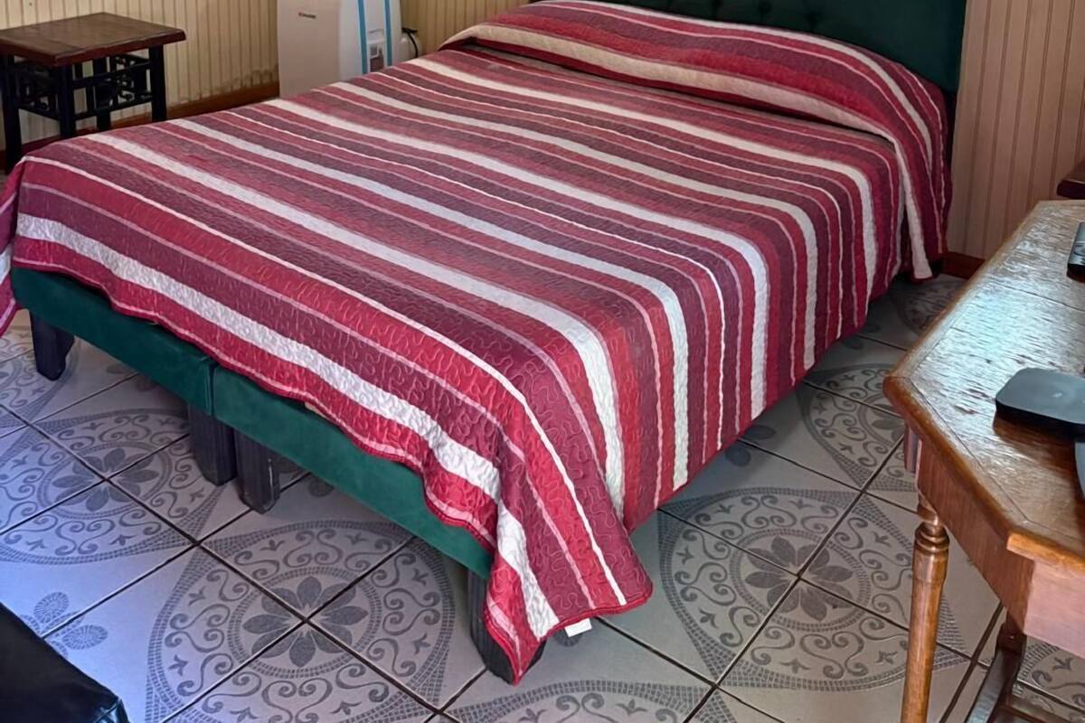 Une chambre à coucher avec un lit, une tête de lit recouverte d’un tissu vert, une table en bois et des carreaux de sol à motifs.