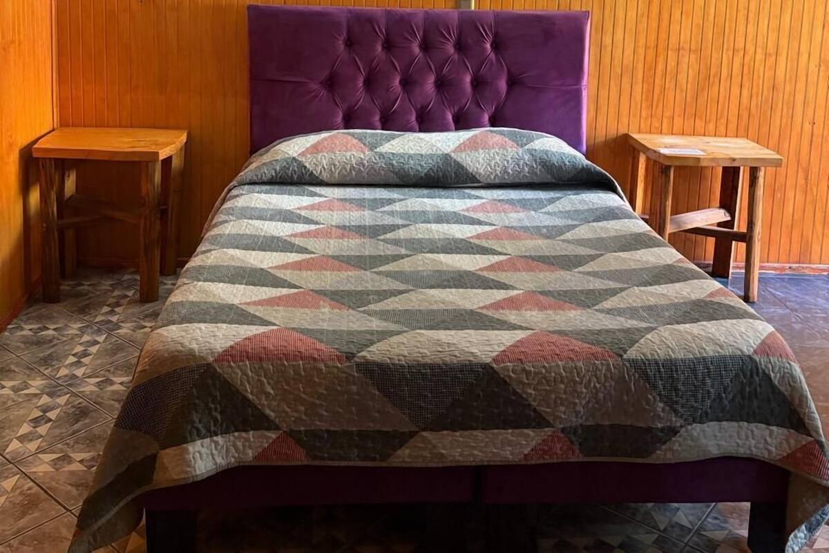 Une chambre avec un grand lit, deux tables de chevet en bois, un luminaire fixé au mur et un tableau.