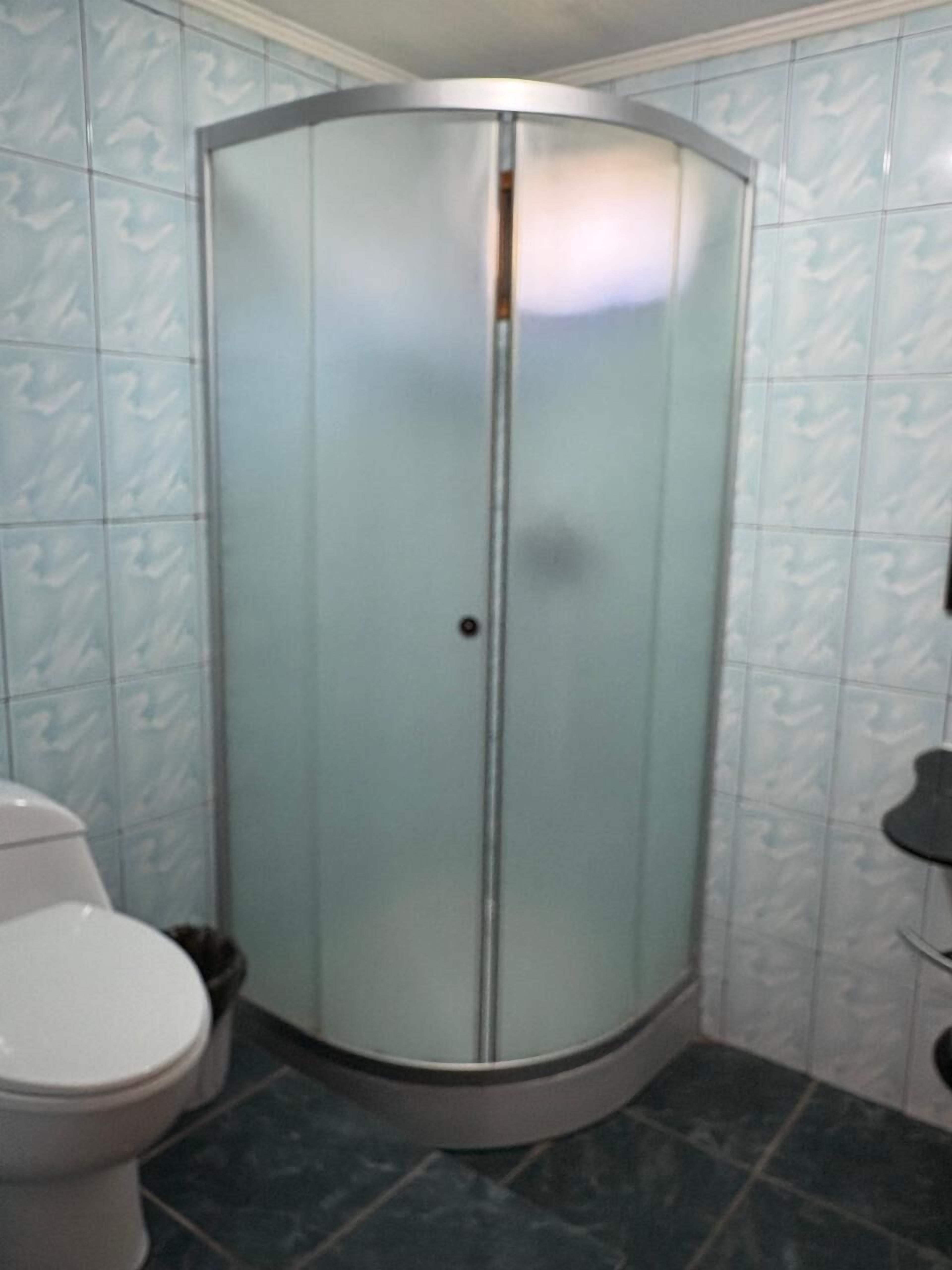 Dusche mit Eckausbau, Glastür, Toilette und Mülleimer.
