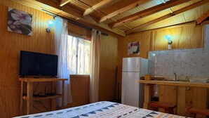 Een knus kamer in een chalet, met een bed, een televisie, een koelkast, een houten bureau en een raam met gordijnen.