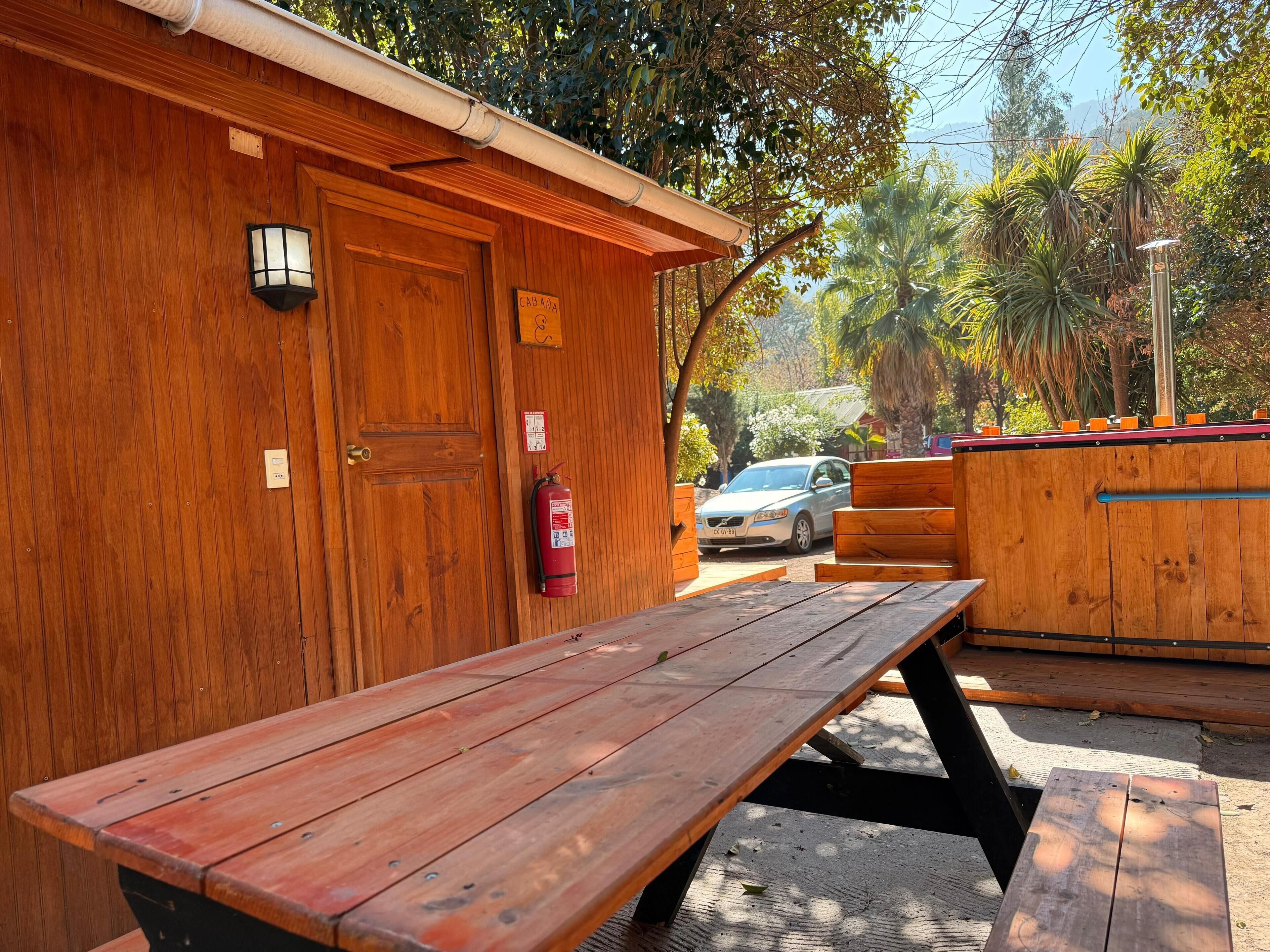 A wooden cabin with a picnic table, a fire extinguisher, and a car parked outside.
