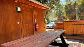 A wooden cabin with a picnic table, a fire extinguisher, and a car parked outside.