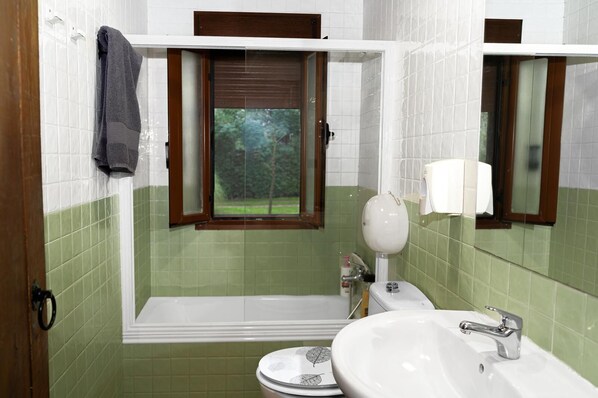 A bathroom with a bathtub, toilet, sink, and a window with a view of greenery. - casa rural la badia (Lucillos)