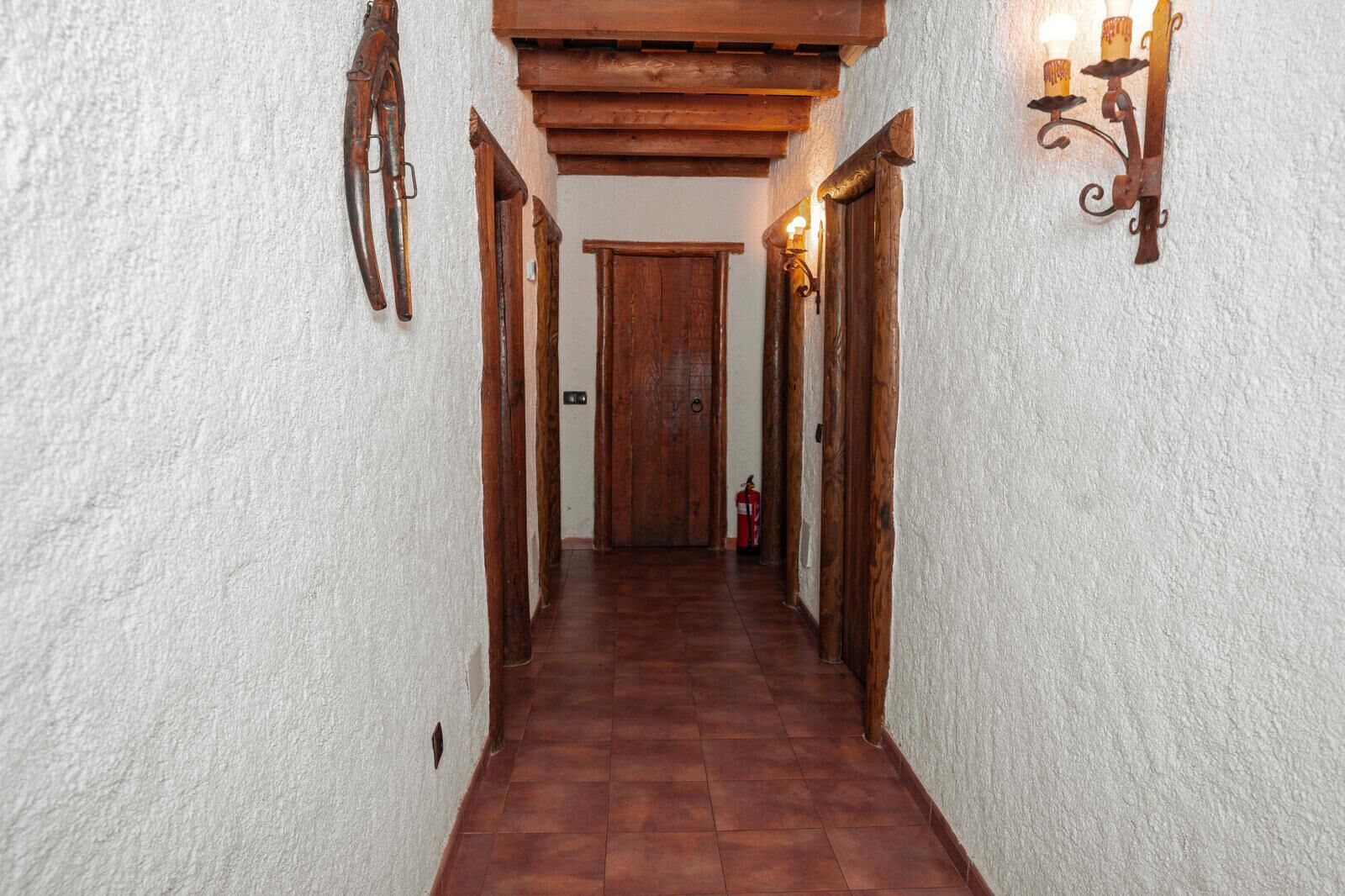 A narrow hallway with wooden doors and a fire extinguisher on the wall.
