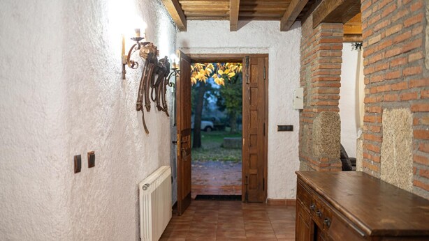 A narrow hallway with white textured walls, a wooden door leading outside, and a rustic wooden counter on the right. - casa rural la badia (Lucillos)