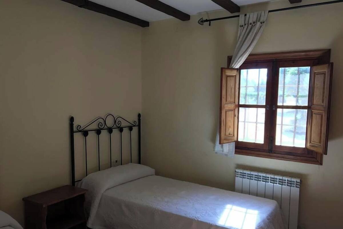 A small, single-bed room with a wooden headboard, a window with wooden shutters, and a radiator.