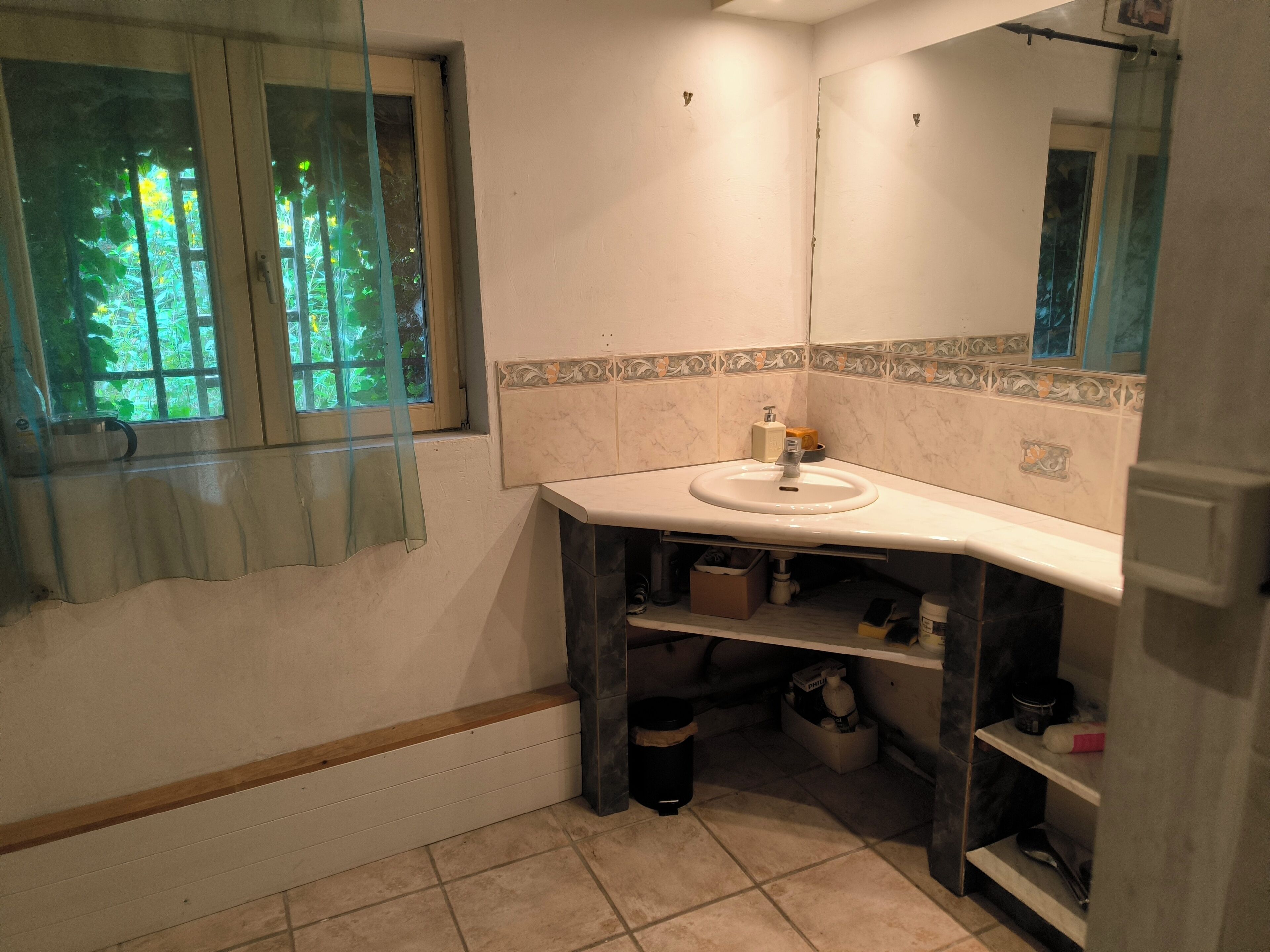 A bathroom with a white sink, a mirror, and a window with a view of greenery.