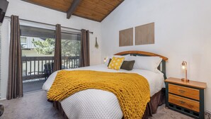 Camera da letto con un letto, una testata in legno, un comodino con una lampada e vista su una terrazza esterna attraverso una porta scorrevole in vetro.