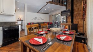 Zona pranzo con tavolo in legno apparecchiato per quattro persone, cucina con lavastoviglie e scala che conduce a un piano superiore.
