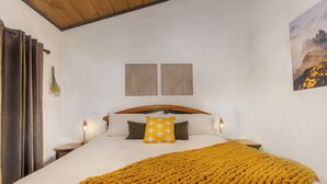 Camera da letto con una testiera in legno, biancheria bianca, una coperta color senape e due pannelli decorativi a parete.