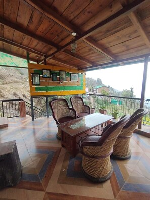 A covered outdoor seating area with a wooden ceiling, a tiled floor, and a table with chairs. - Luxsugero Moonlight (Bhimtal)
