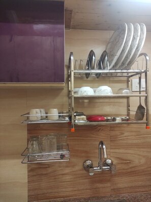 A kitchen with a dish rack holding plates, bowls, and cups, a sink with a faucet, and a cabinet above. - Luxsugero Moonlight (Bhimtal)