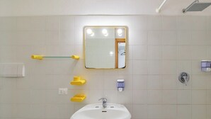 A bathroom with a white sink, a mirror with lights, a showerhead, and yellow soap dispensers.