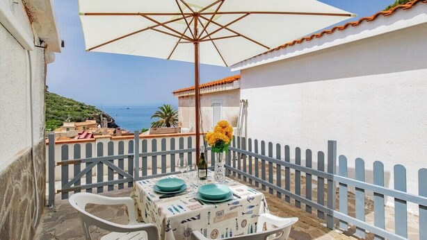 A terrace with a table set for two, a white umbrella, and a view of the sea.