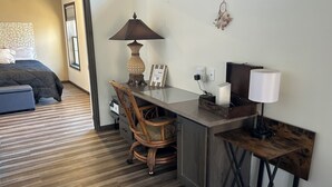 Habitación de hotel pequeña con cama, escritorio con silla, lámpara y mesita.