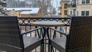 A balcony with wicker chairs and a small round table, overlooking a snowy landscape with buildings and trees. - Lift House Lodge, Downtown Vail Lionshead Village Studio Condo (Vail)