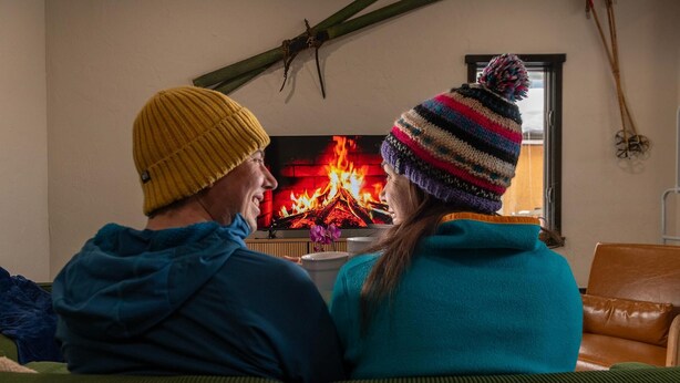 Two people sitting on a couch facing a fireplace with a visible fire. - Lift House Lodge, Downtown Vail Lionshead Village Studio Condo (Vail)